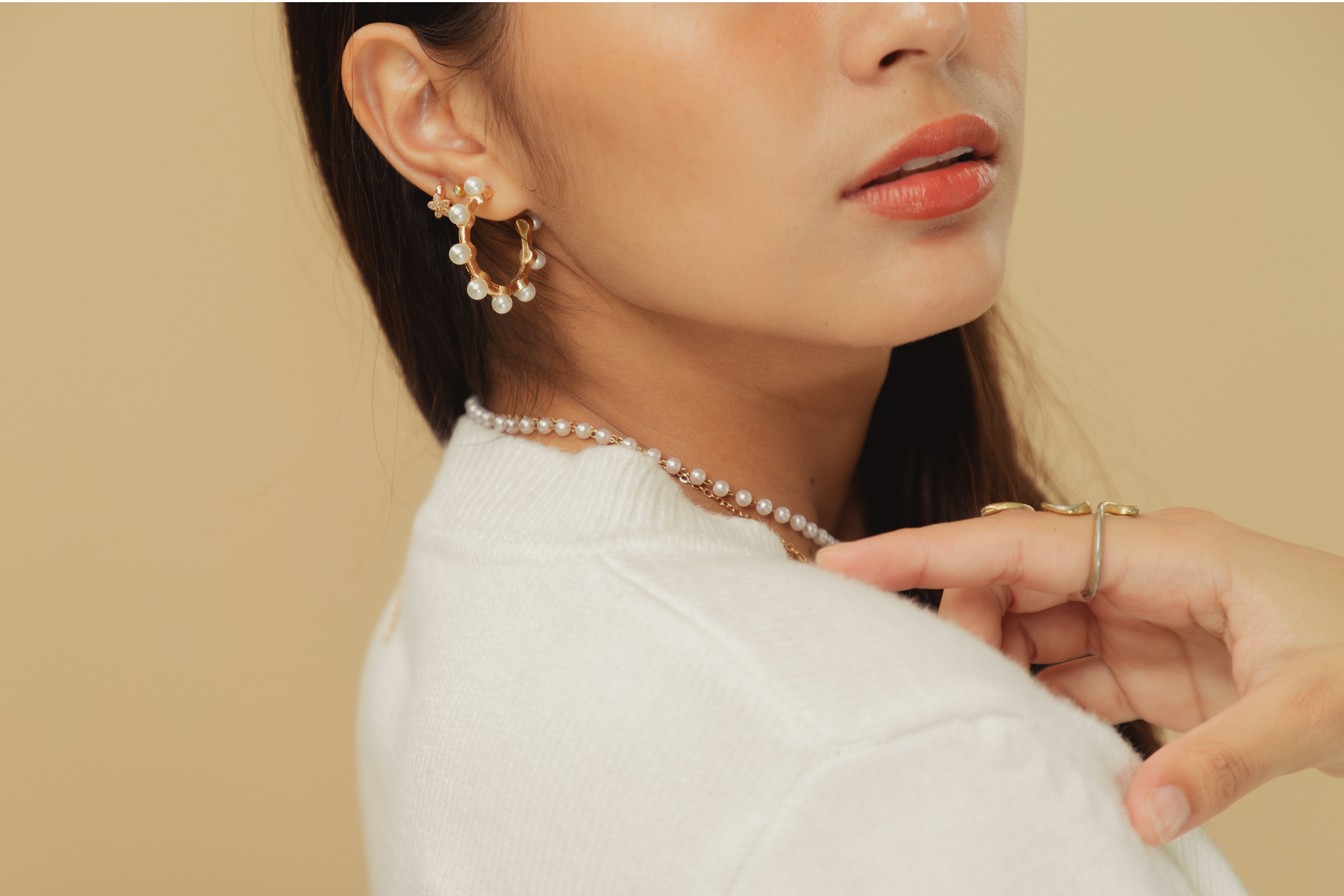 Close-up of a woman wearing pearl earrings and a necklace against a beige background